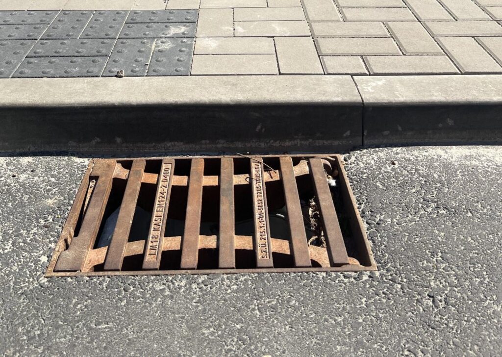 Litinová mříž uliční vpusti KASI třídy D400 u obrubníku, sídliště Dubina Pardubice